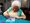 Eine weisshaarige Frau sitzt an einem Tisch und malt ein Bild mit Wasserfarben.
