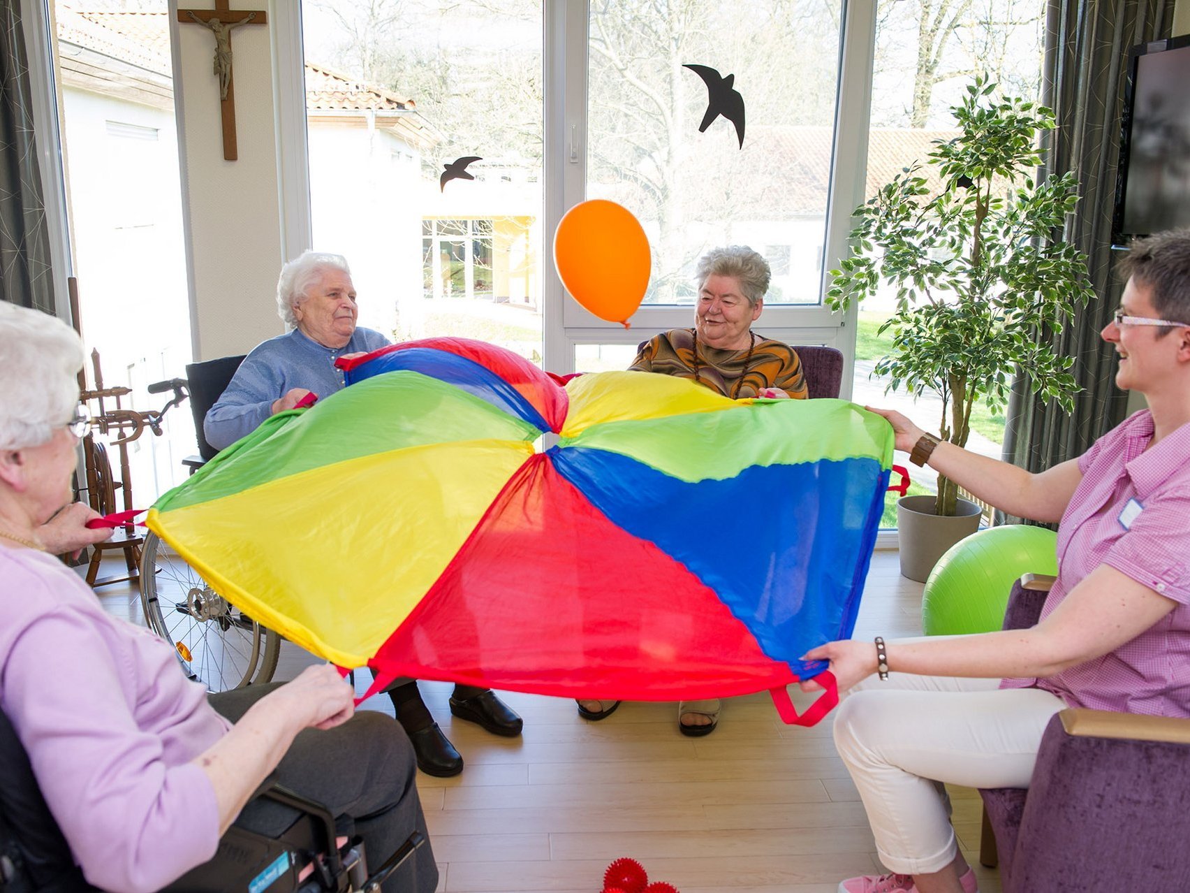 Bewohner sitzen im Kreis und spielen mit einem bunten Tuch und einem Luftballon 