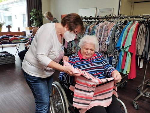 Einer Frau im Rollstuhl wird ein Pullover von einer Verkäuferin gezeigt