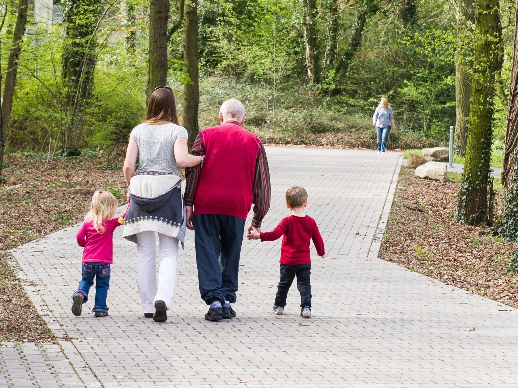 Familie beim Spazierengehen im Park: Die Enkelin stützt ihren Großvater zwei Kinder gehen jeweils an der Hand