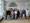 Eine Gruppe von etwa 16 Erwachsenen posiert in einem hellen Raum mit Holzboden für ein Gruppenfoto. Im Hintergrund ist eine große Tür mit einem Kreuz darüber zu sehen. Die Personen tragen legere Kleidung.